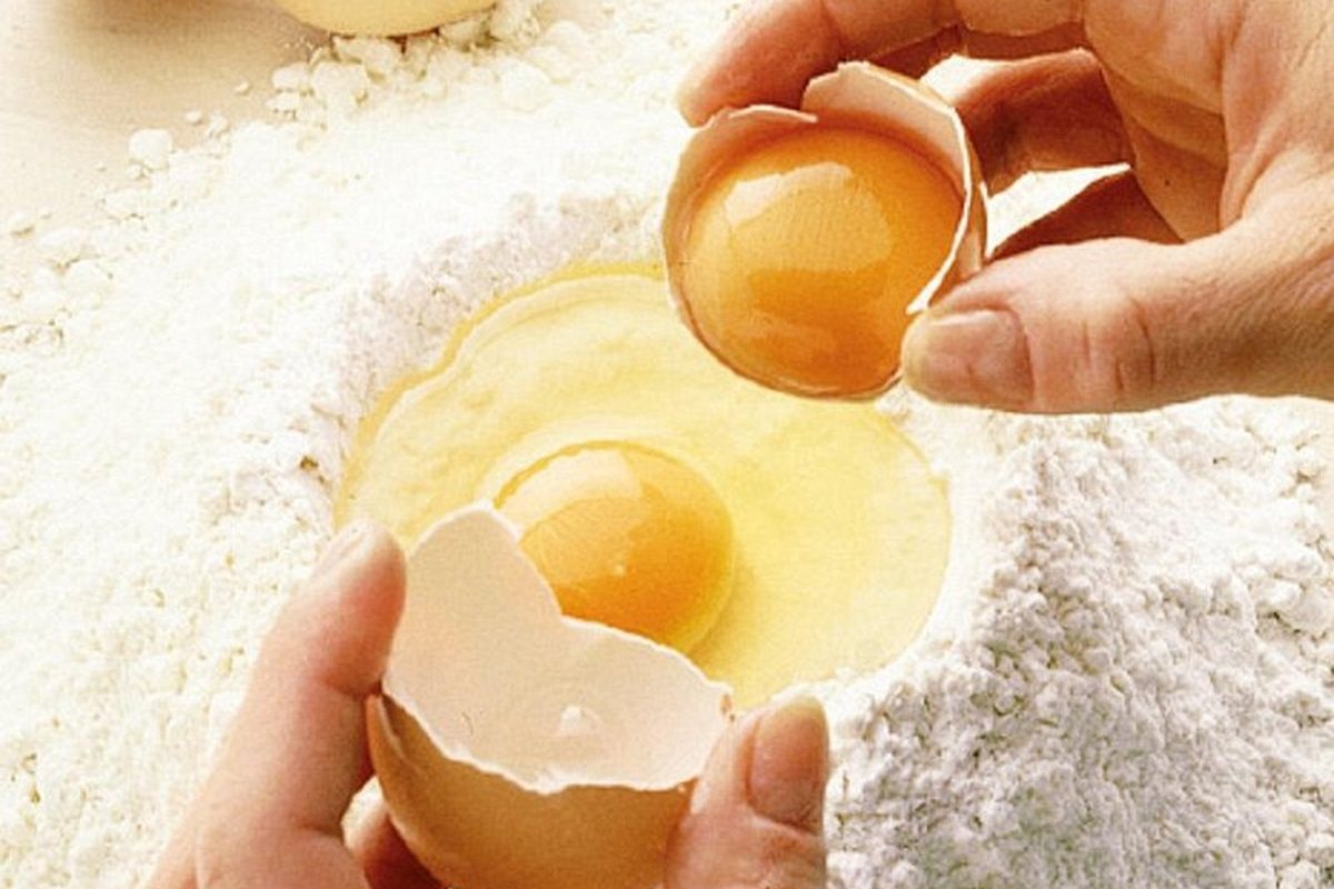 An egg cracked into a well of flour at the start of a pasta class