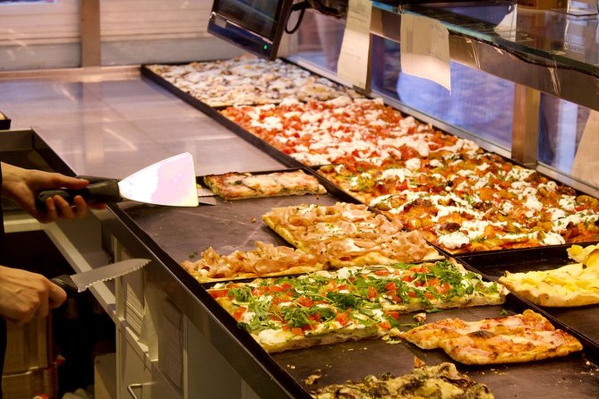 The counter of a Roman pizza al taglio shop, trays laid out under glass