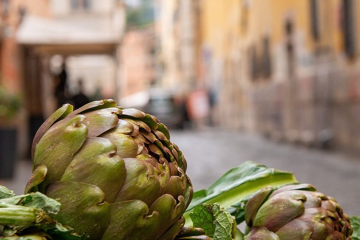 Roman artichokes stacked on a market stall with a Rome street behind them