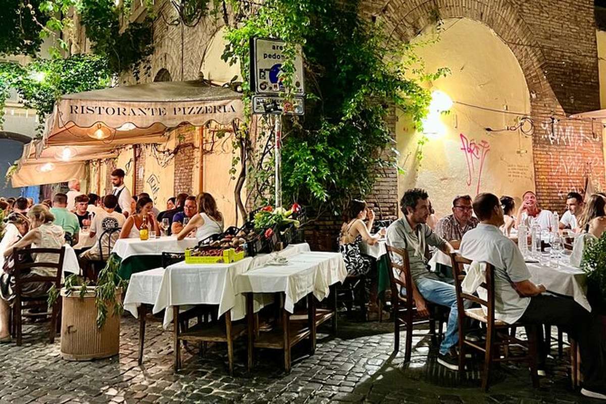 Tables set out under vines on a Trastevere lane after dark